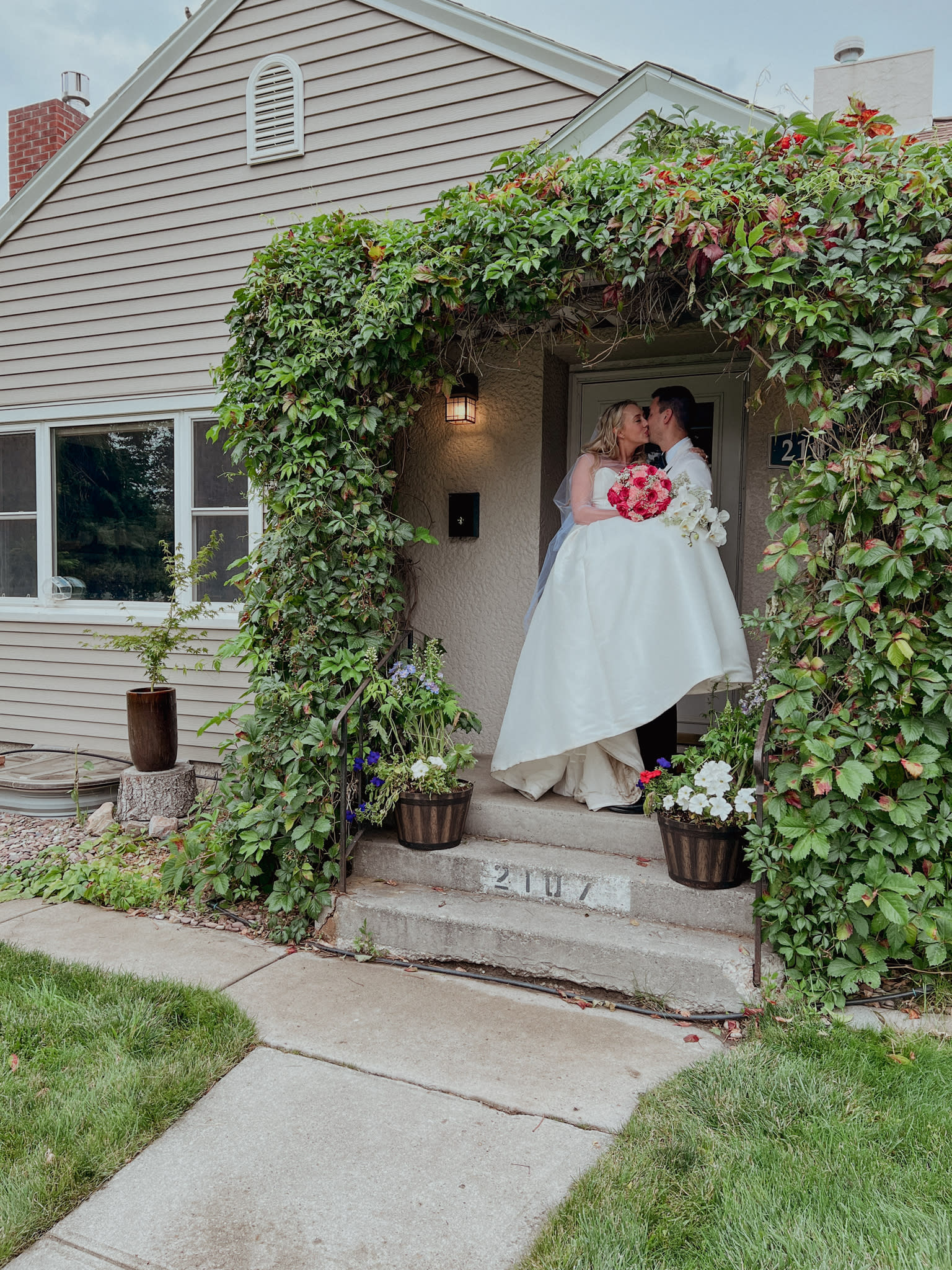 image shows a bride and groom posing under a leafy green treliis