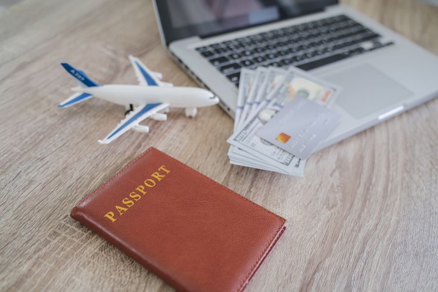 image shows a small airplane, passport book, money, and a laptop insinuating travel planning