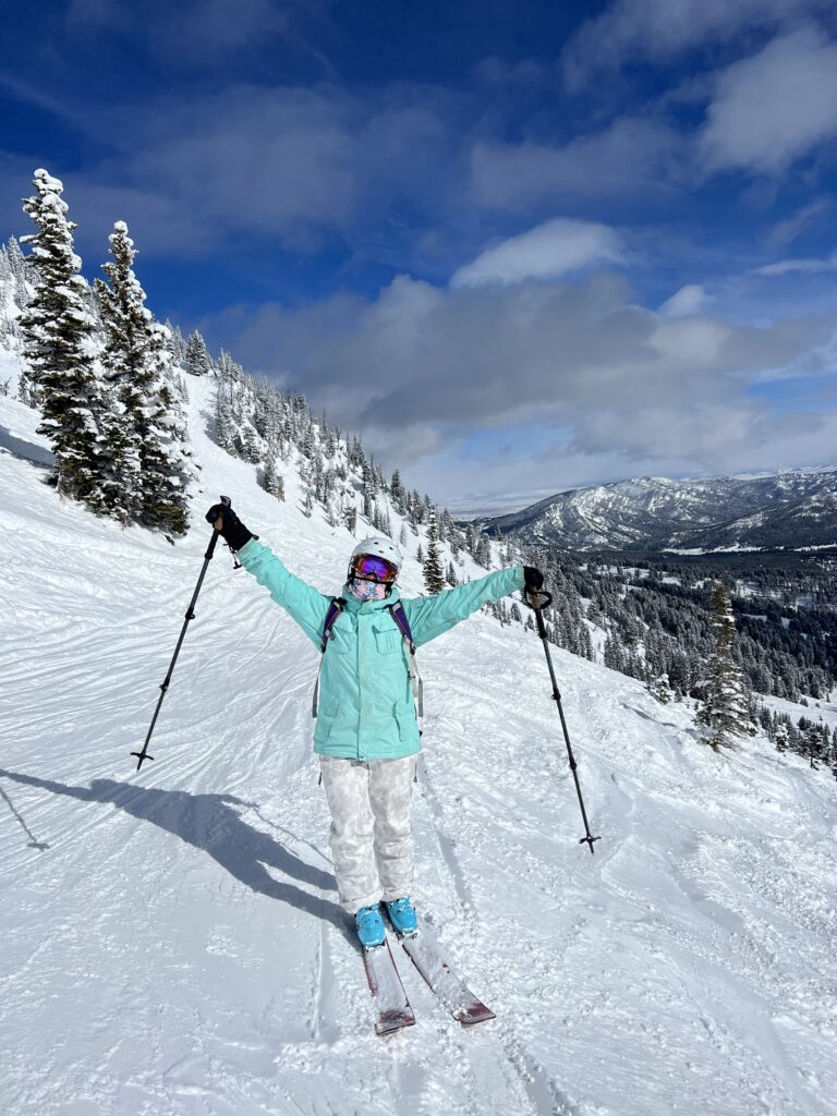 this image shows a skiier wearing blue and white, posing with their hands up 