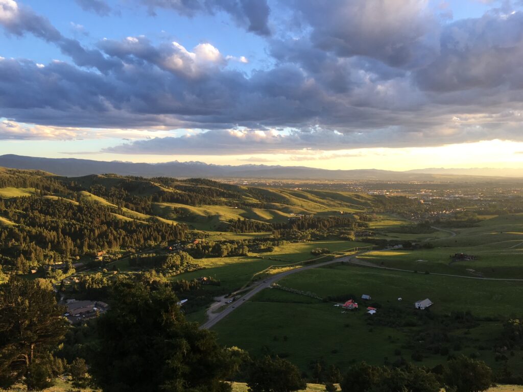 image shows  a view of green foothills at sunset with the contrast of a blue sky