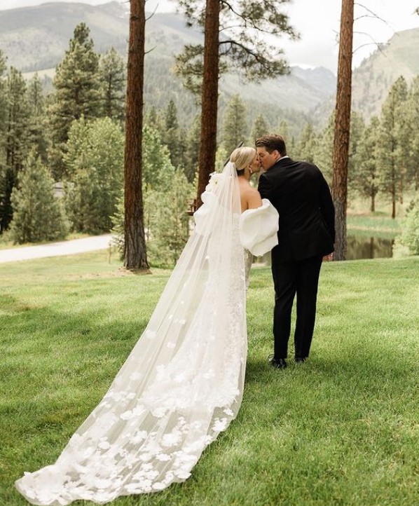 a bride and groom face away looking toward the trees and mountains while they share a kiss. 