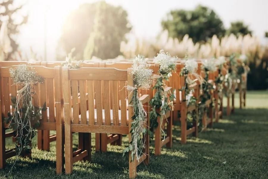 image shows seating for an outdoor ceremony decorated with floral arrangements