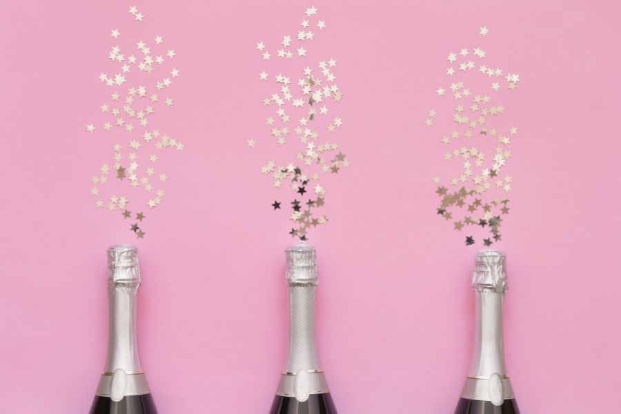 image shows champagne bottles against a pink background with glitter