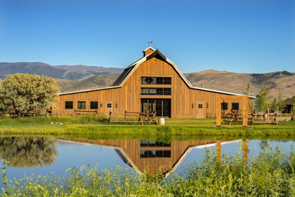 image shows a wedding barn reflected by a small pond in the foreground and rolling hills in the background