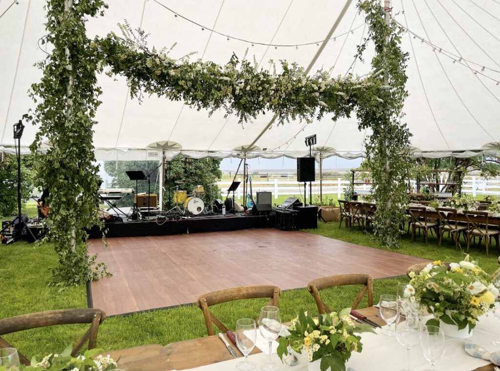 image shows a beautiful wedding event tent with a dance floor and decorated with lush greenery