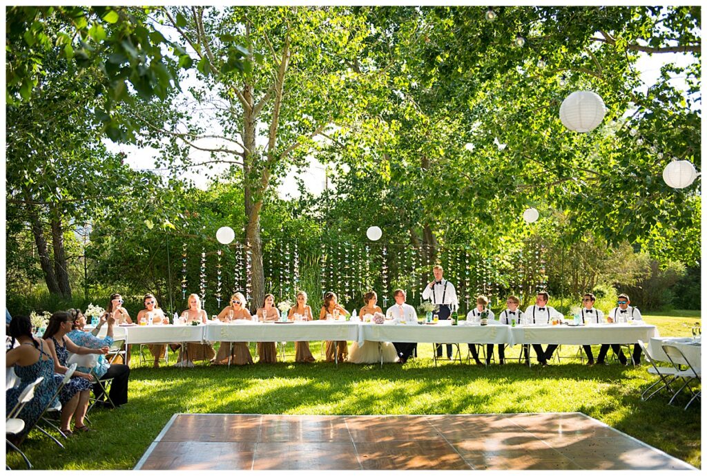 image  shows a wedding party seated at a table in an outdoor reception