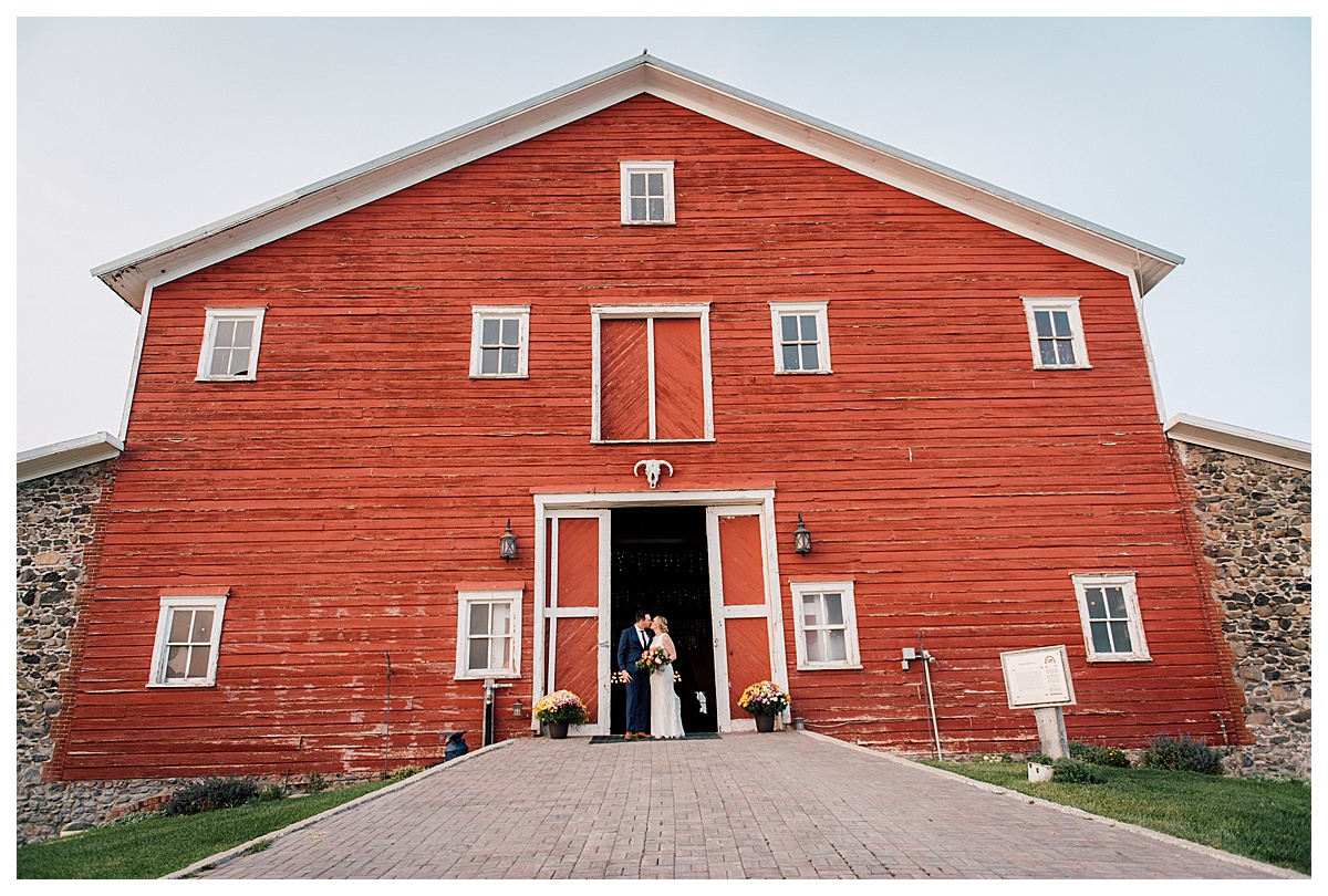 image shows a couple sharing a kiss in front of a big red barn