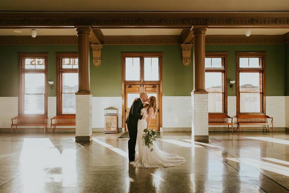 image shows a bride and groom sharing a kiss in a large room