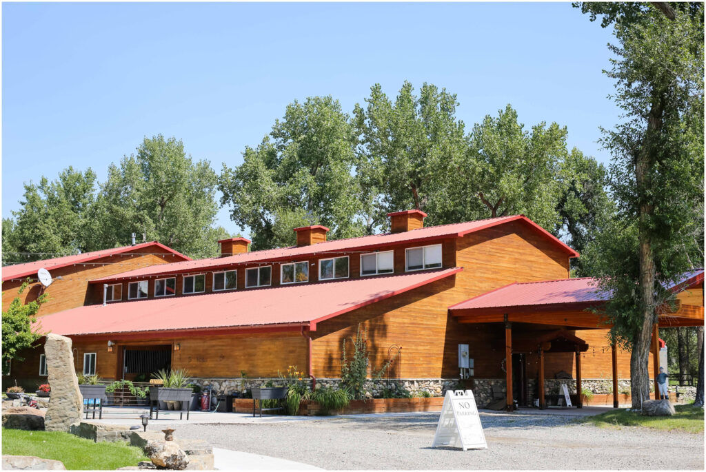 image shows a large wedding barn with a red roof surrounded by trees and a large outdoor area